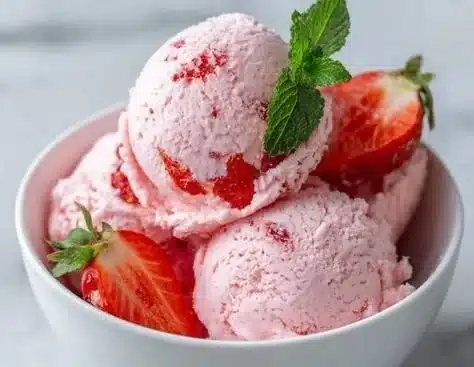 Delicious homemade strawberry ice cream in a bowl with fresh strawberries.